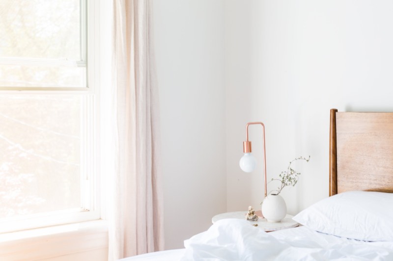 A bright bedroom with strong daylight through a large window, the kind of room that overheats in summer